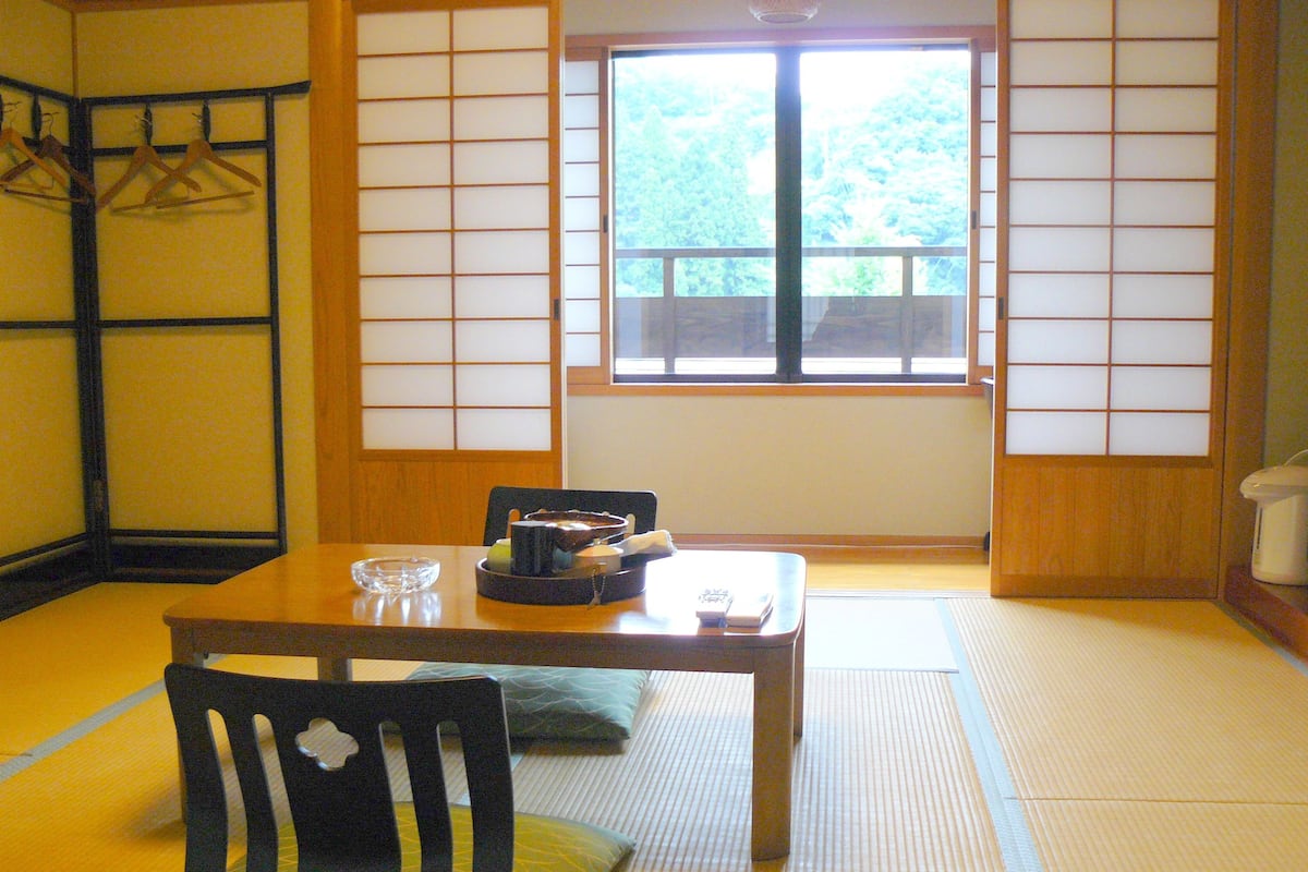 A traditional Japanese room with tatami flooring, a low table, a chair, and a sliding shoji screen door.