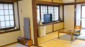 Una habitación japonesa tradicional con suelo de tatami, una mesa baja, un televisor y un calentador.