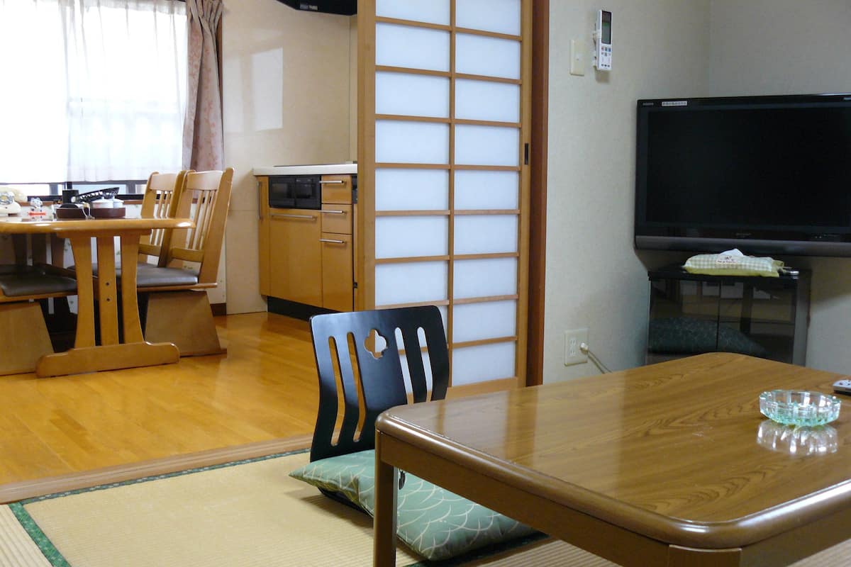 A traditional Japanese-style room with tatami flooring, a low wooden table, and a television on a stand.
