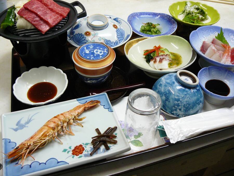 A variety of dishes and condiments on a table, including a plate with a cooked shrimp and star anise, bowls of soup, and plates with vegetables and meat.