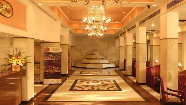 A hotel reception area with a chandelier, marble flooring, and red upholstered chairs. - Tuli International (Nagpur)