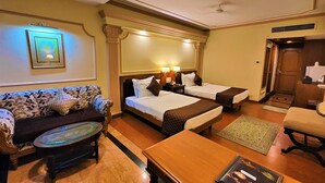 A hotel room with two beds, a sofa, a coffee table, and a small table with a magazine. - Tuli International (Nagpur)