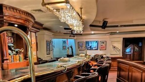 A bar area with a long counter, multiple stools, and a decorative mirror. - Tuli International (Nagpur)