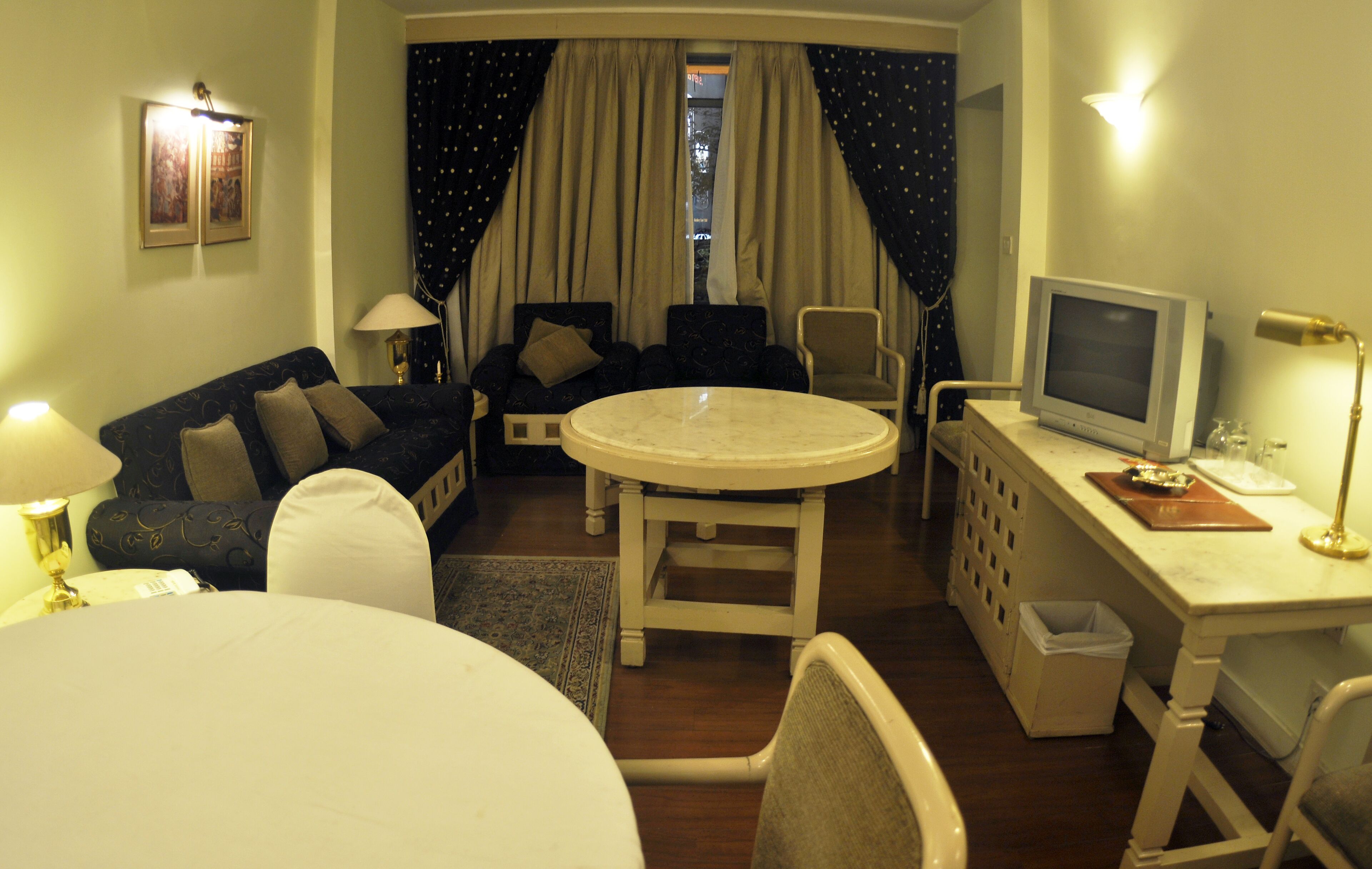 Een hotelkamer met een ronde eettafel, een bank, een televisie en een bureau.