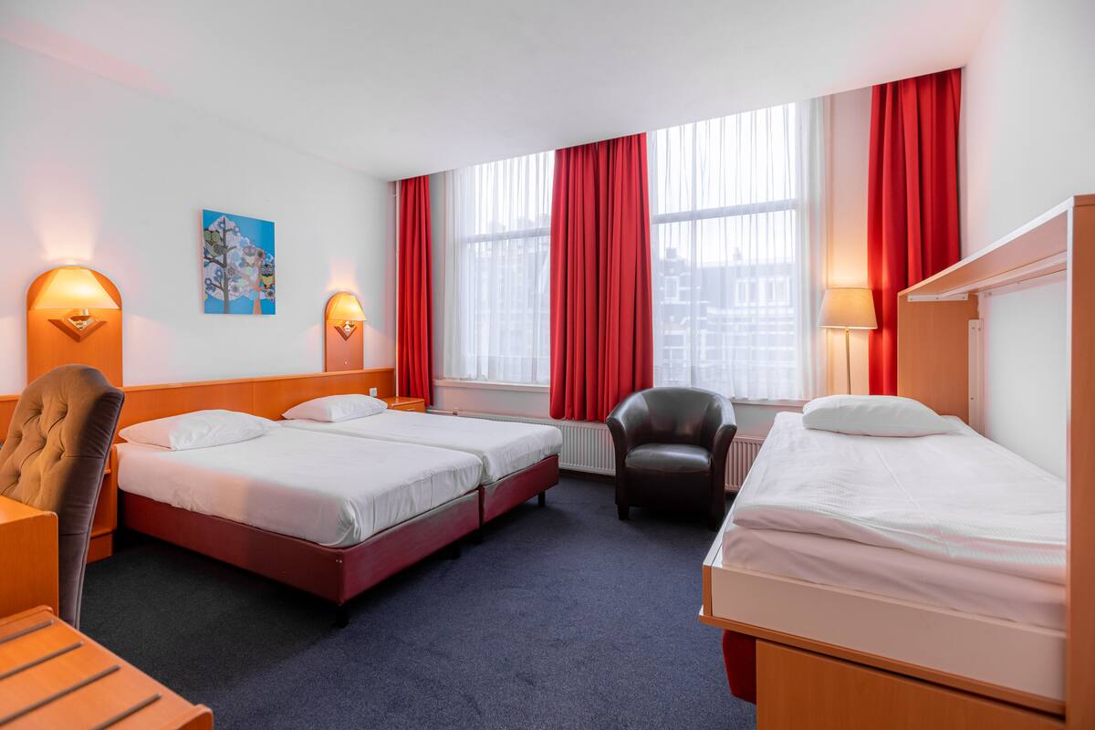 A hotel room with two beds, a desk, a chair, and a radiator.