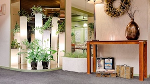 A lobby with a mirror, potted plants, a wooden console table with a vase, a lamp, a wreath, and a framed picture. - Owl Hotel (Amsterdam)