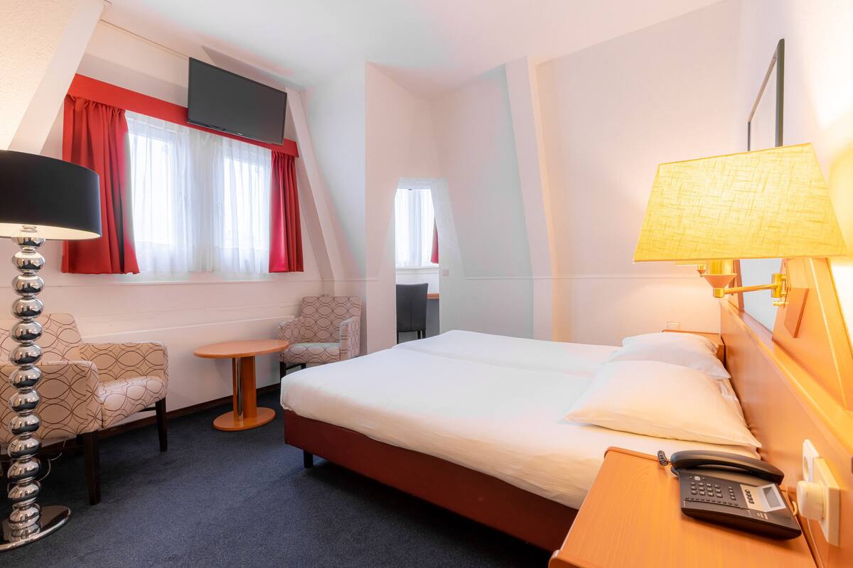 A hotel room with a bed, a desk, a chair, a lamp, and a telephone.