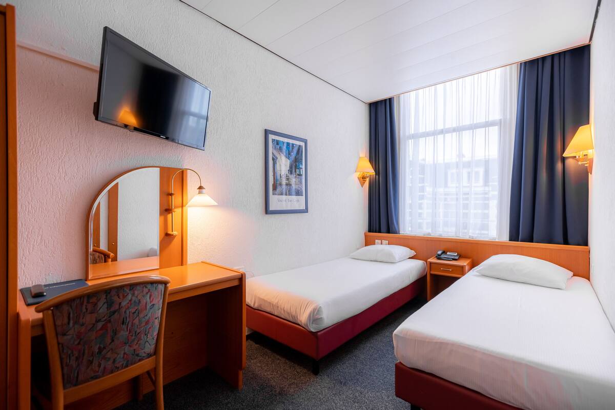 A hotel room with two beds, a desk, a chair, a TV, and a window with curtains.