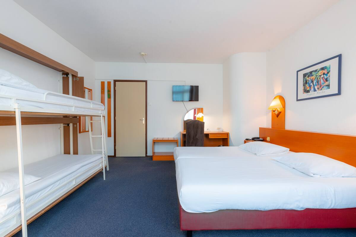 A hotel room with bunk beds, a desk, a chair, a lamp, and a painting on the wall.