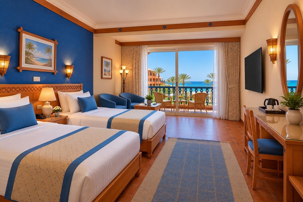 A hotel room with two beds, a desk, a chair, a TV, and a balcony with a view of the sea.