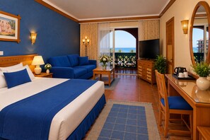 A hotel room with a large bed, a sofa, a desk with a chair, a TV, and a balcony with a view. - Dreams Beach Marsa Alam (El Quseir)