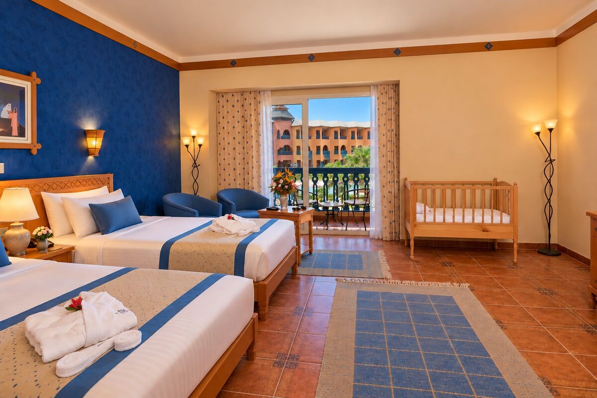 A hotel room with two beds, a balcony, and a view of buildings.