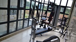 Et fitnesscenter med træningsudstyr, store vinduer og udsigt til det fri.