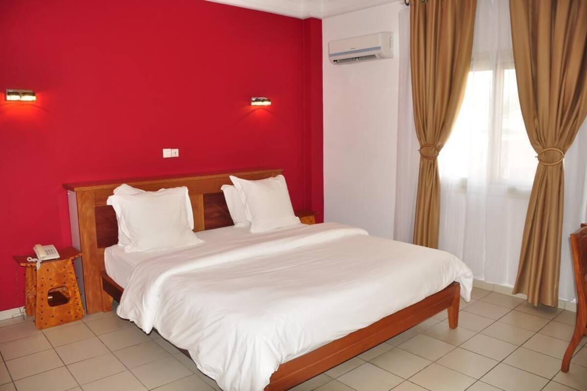 A hotel room with a wooden bed, red walls, and beige curtains.