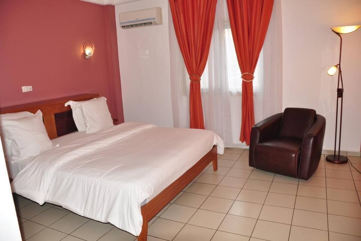 A hotel room with a bed, a chair, a floor lamp, and curtains.
