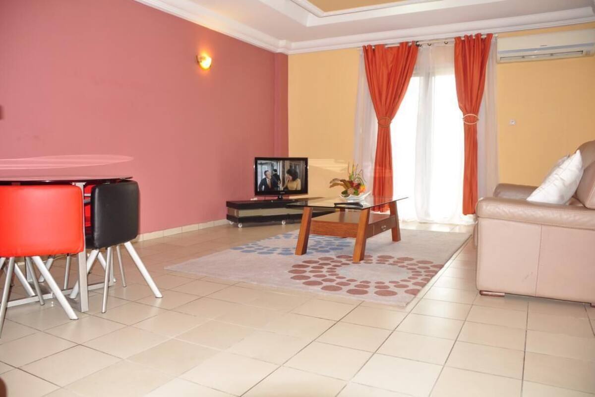 A living room with a red table, black chairs, a beige sofa, and a TV.