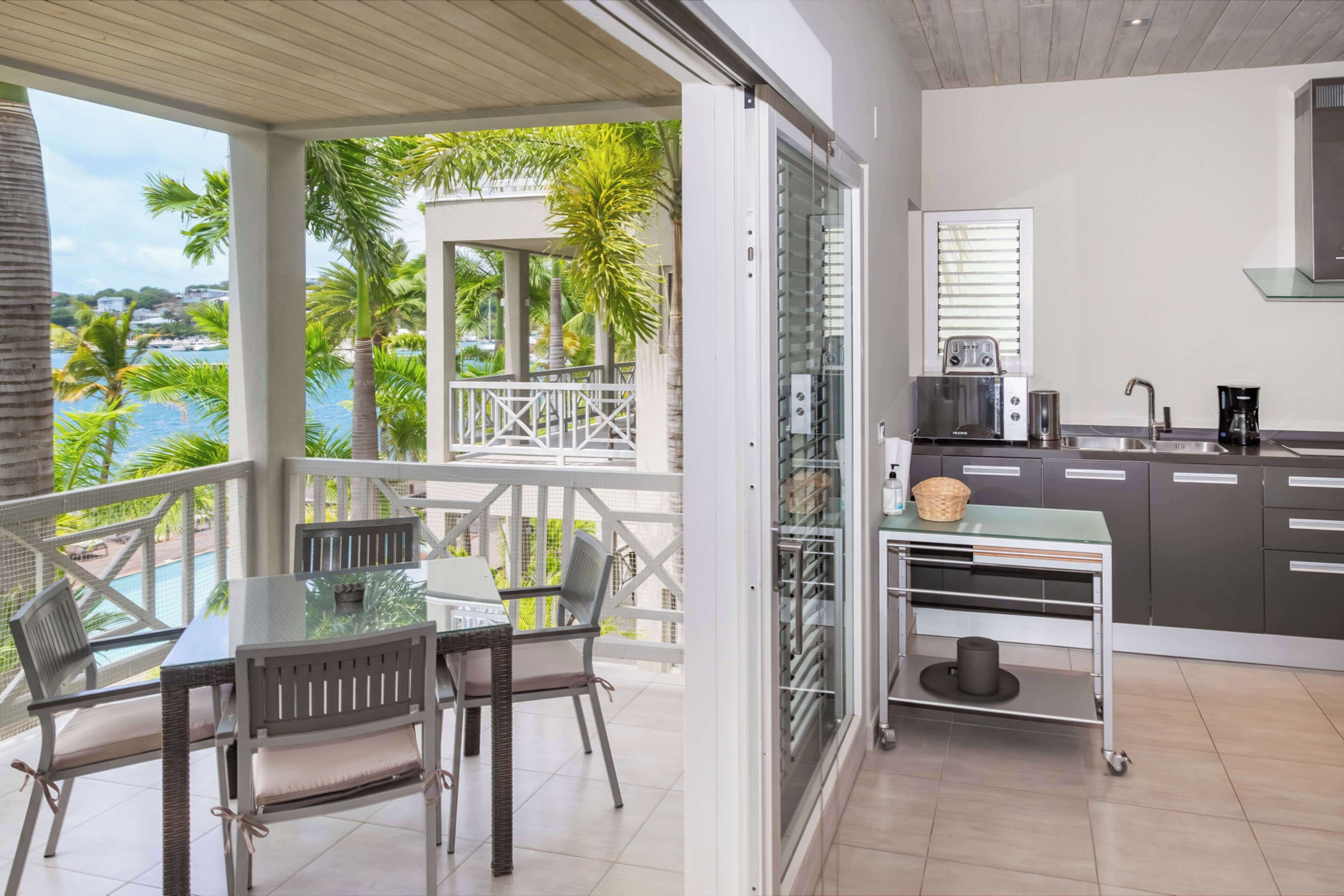 A balcony with a table and chairs, a kitchen with a sink and cabinets, and a view of the sea.