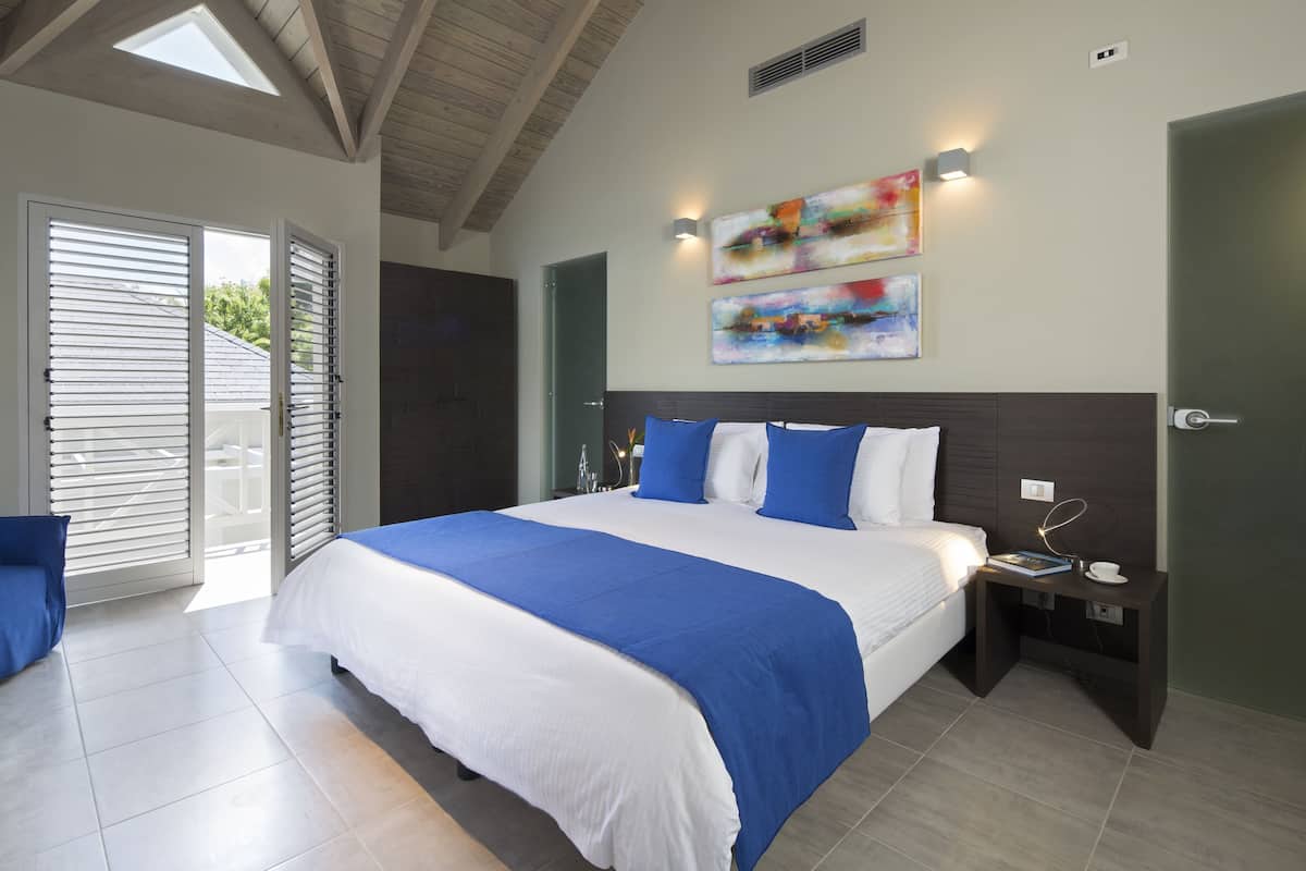 A bedroom with a large bed, a nightstand, a wall-mounted light, and a sliding glass door leading to an outdoor area.