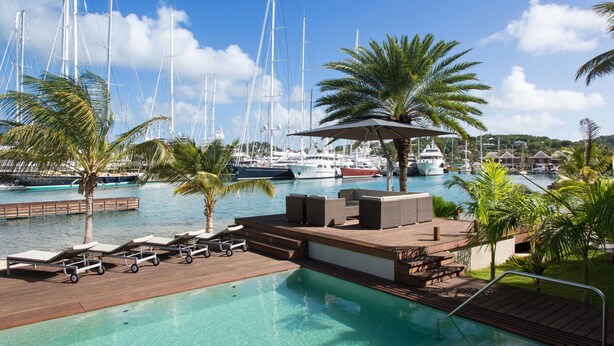 A marina with boats, a pool area with lounge chairs, and palm trees. - South Point Antigua Ocean Suites (English Harbour)