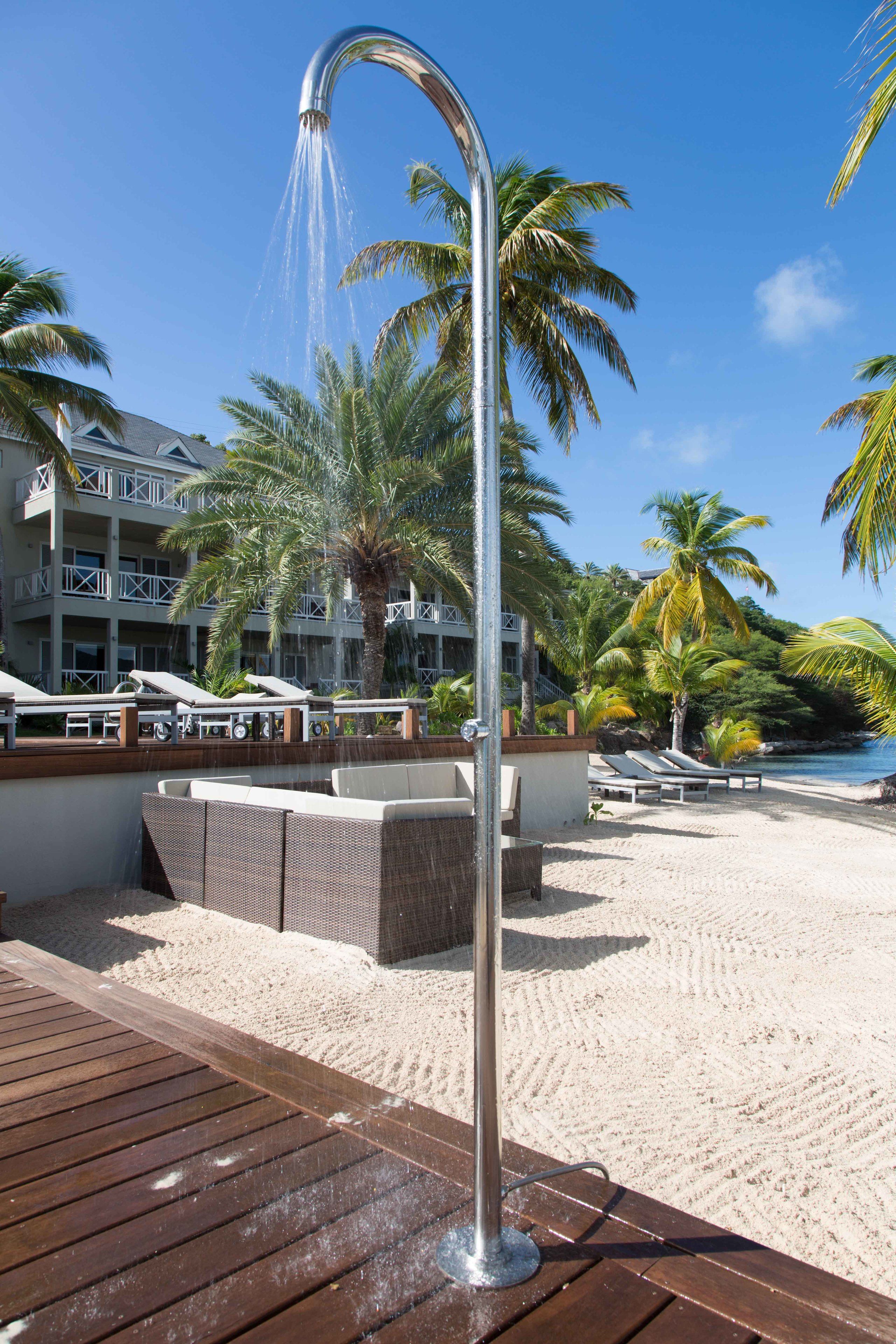 A beachside shower with a view of a resort building and palm trees.