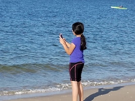 Una persona parada en la playa, mirando un teléfono inteligente.