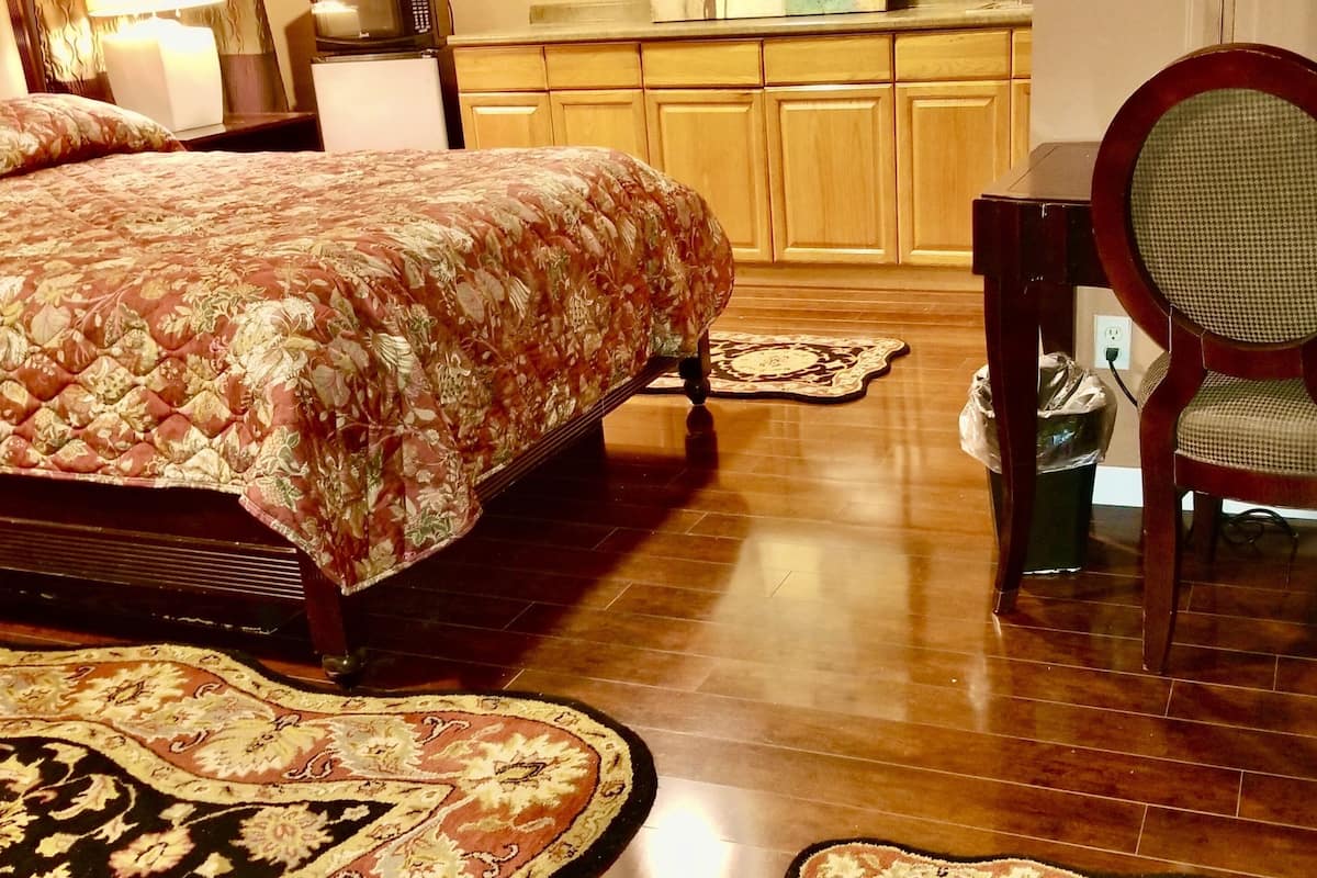 Een slaapkamer met een bed, een stoel, een bureau en een keuken in de verte.