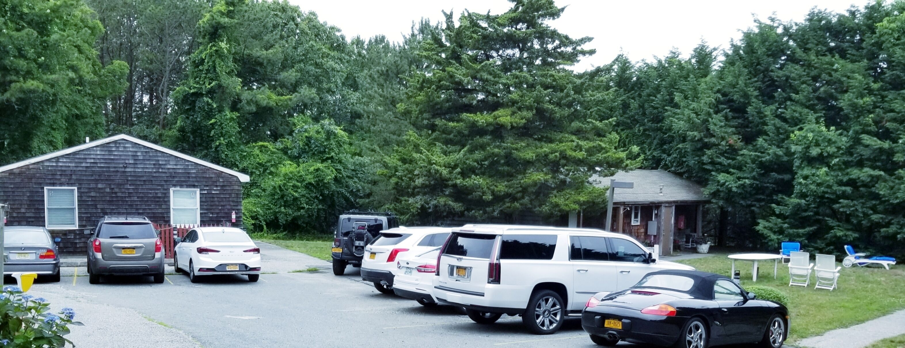 A parking lot with several cars, a small building, and a lawn with chairs.