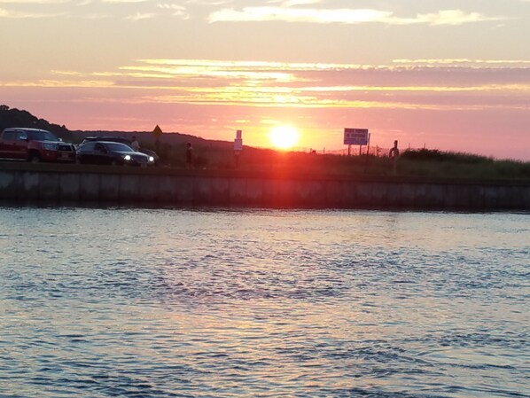 A sunset over a body of water with a bridge and vehicles in the foreground.
