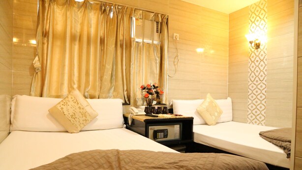 A hotel room with two single beds, a bedside table with a phone and a vase of flowers, and a wall-mounted light fixture. - New Tokyo Hostel (Kowloon)