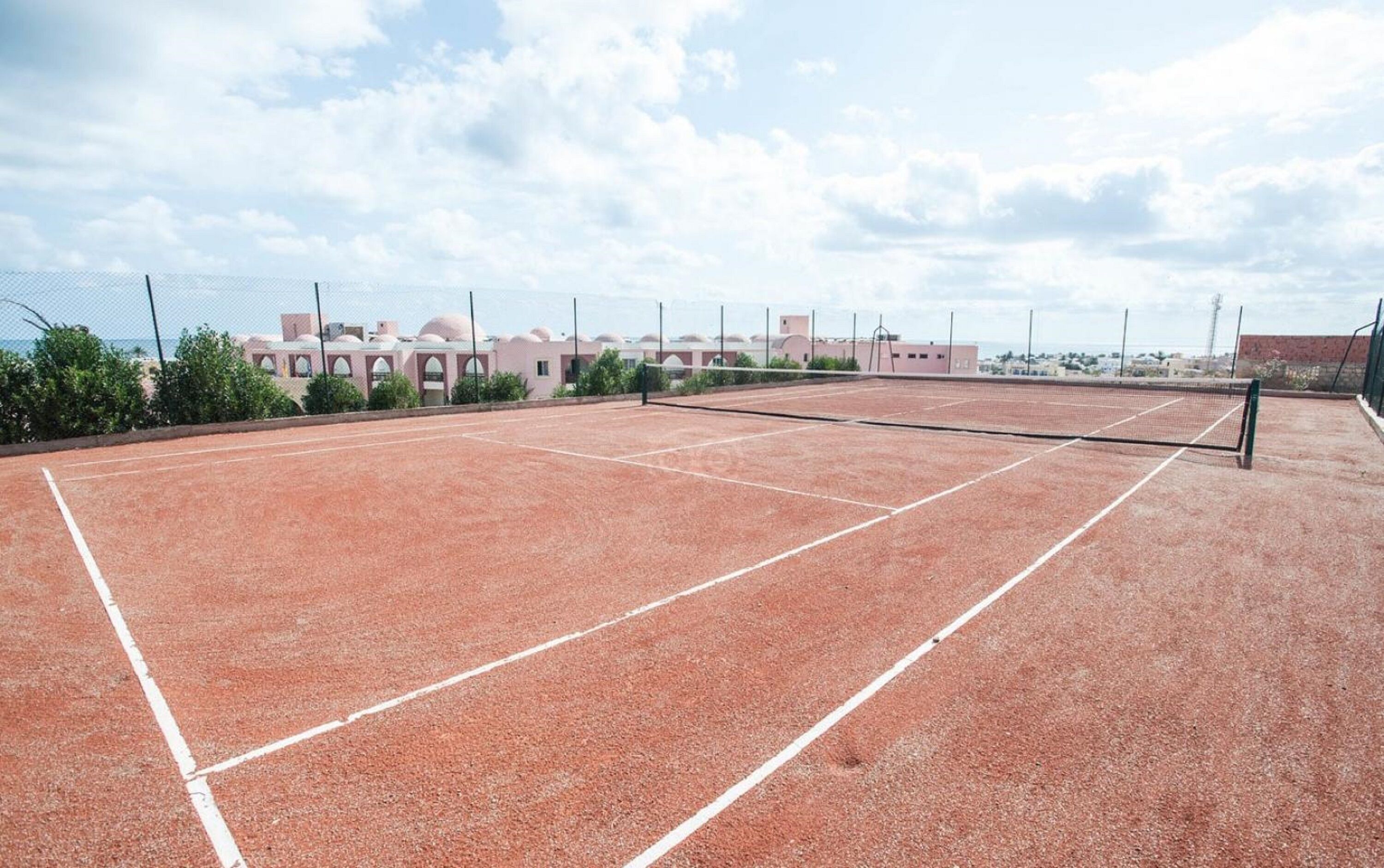 Ein Tennisplatz im Freien mit Netz, umgeben von Gebäuden und Grünflächen.