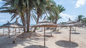 Una playa con palmeras y sombrillas de paja.