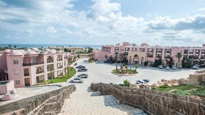 Un resort con edificios de color rosa, un patio central y vista al mar.