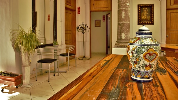 A wooden table with a decorative ceramic vase, a potted plant, and a metal chair in a room with white walls and wooden doors. - Hostel Lit (Guadalajara)