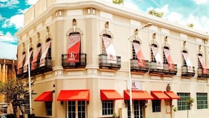 A corner building with multiple balconies, red awnings, and a sign with a red and white logo. - Hostel Lit (Guadalajara)