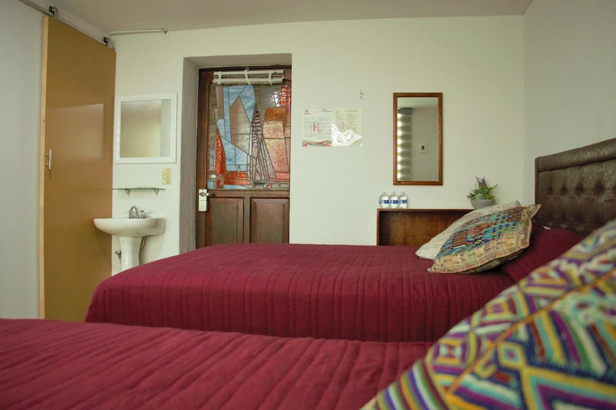 A room with a bed, a bedside table, a mirror, a window with a view, and a door.