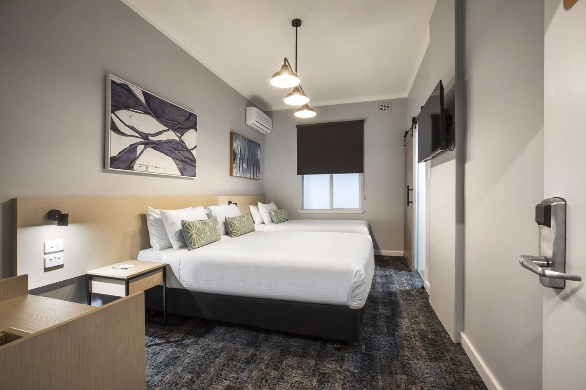 A hotel room with a large bed, a desk, a chair, a TV, and artwork on the walls.