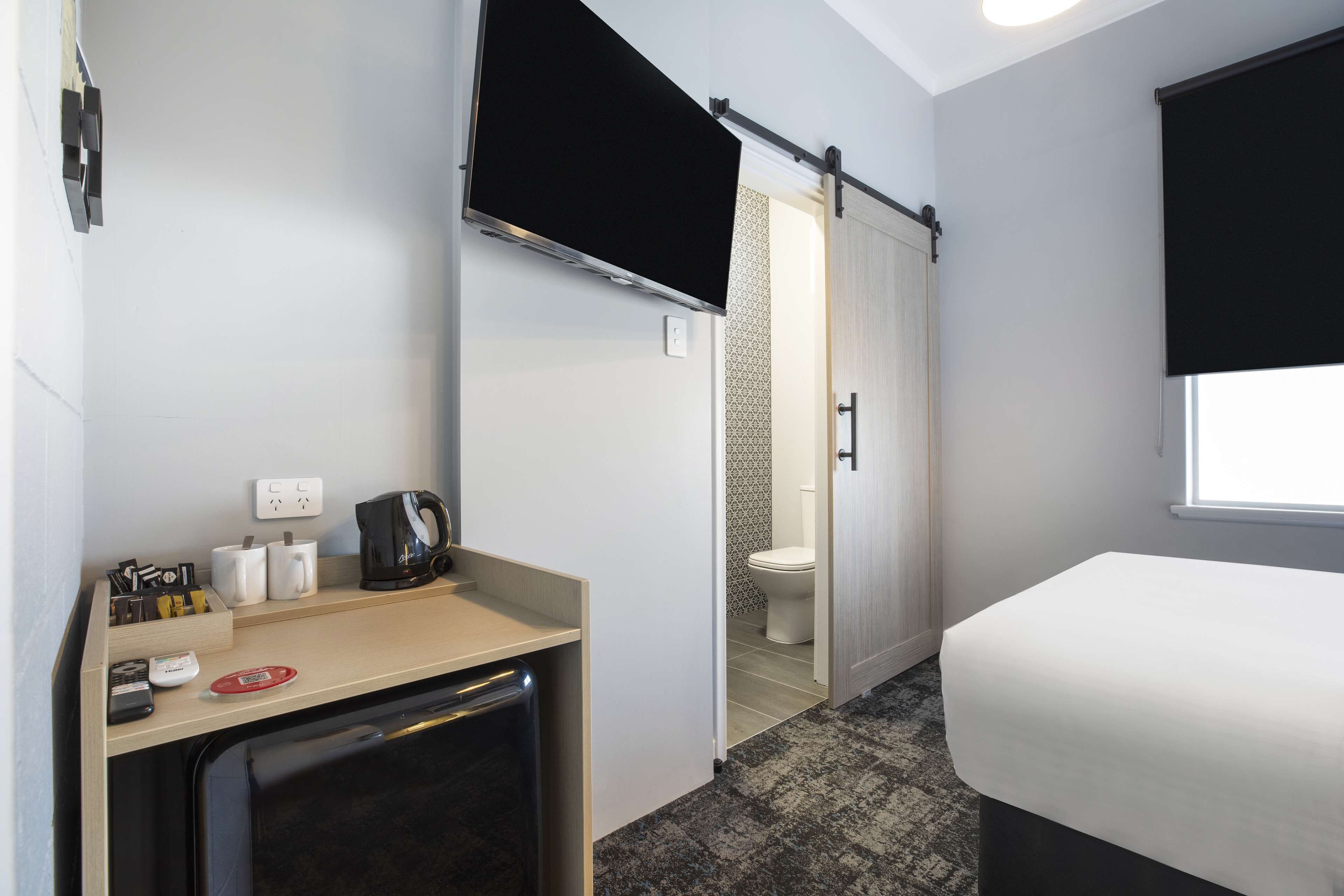 A hotel room with a bed, a desk with a coffee maker, a TV, and a shower area.