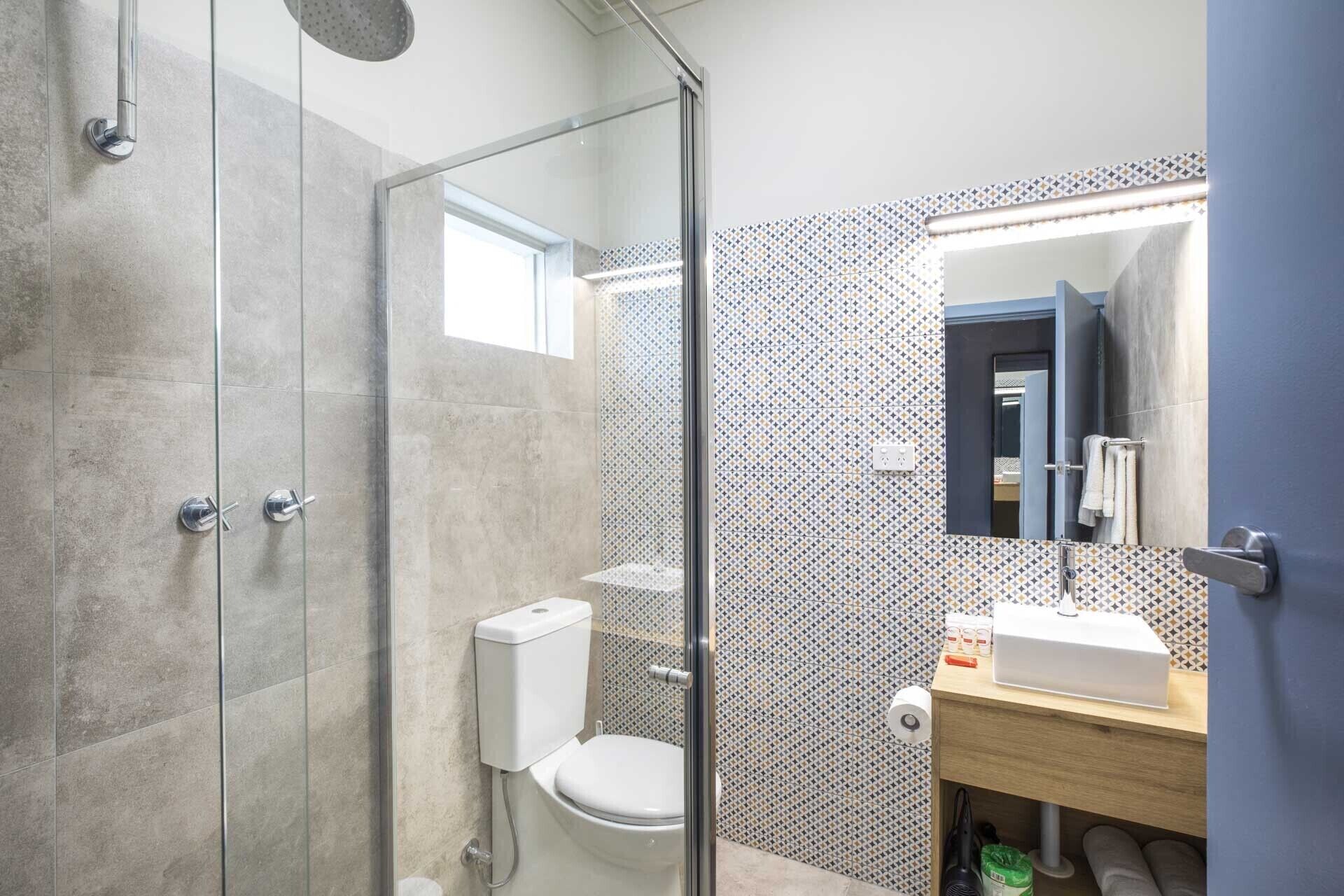 A bathroom with a glass shower enclosure, a toilet, and a sink with a mirror above it.