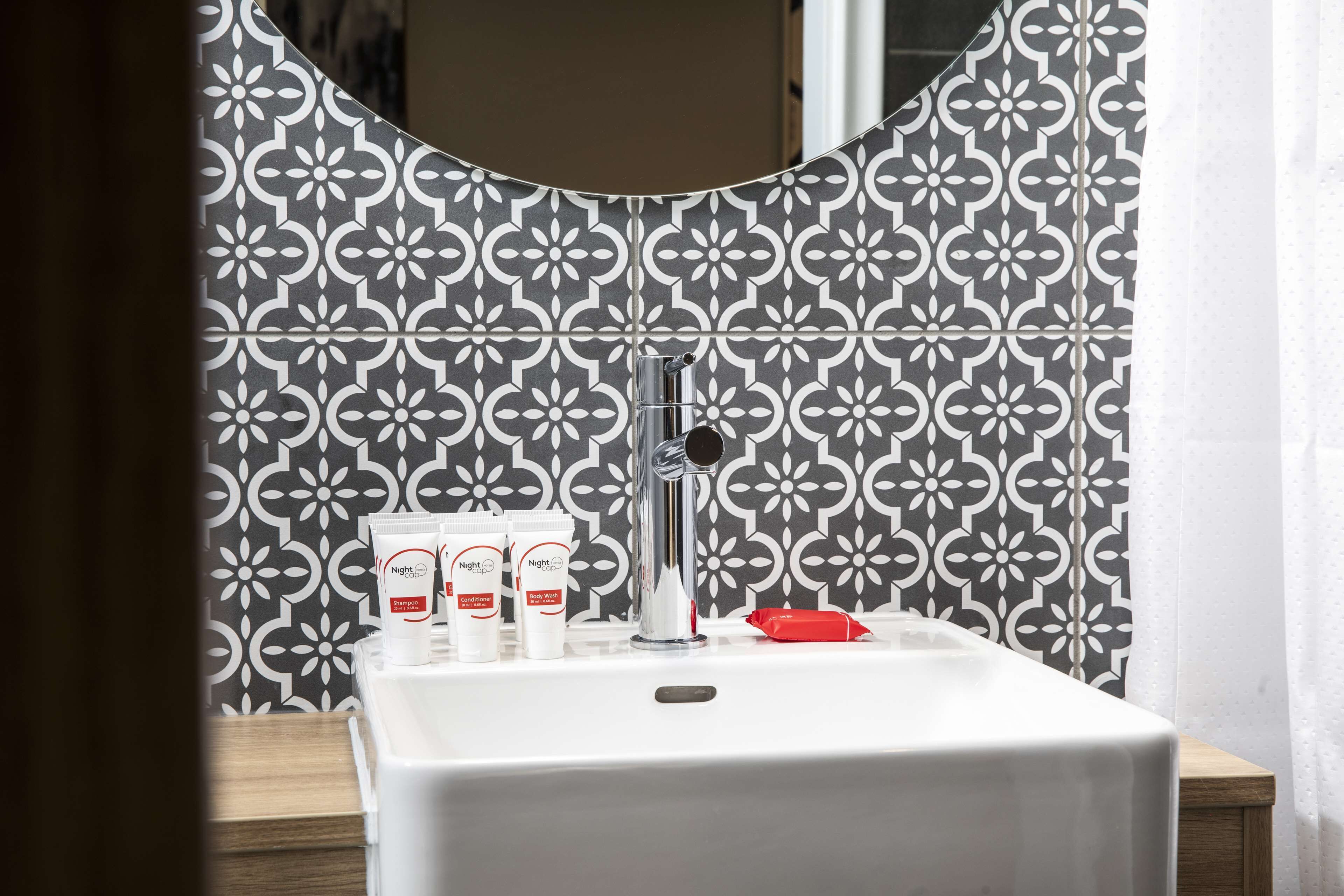 Un baño con un lavabo blanco, un espejo y una pared con diseño.