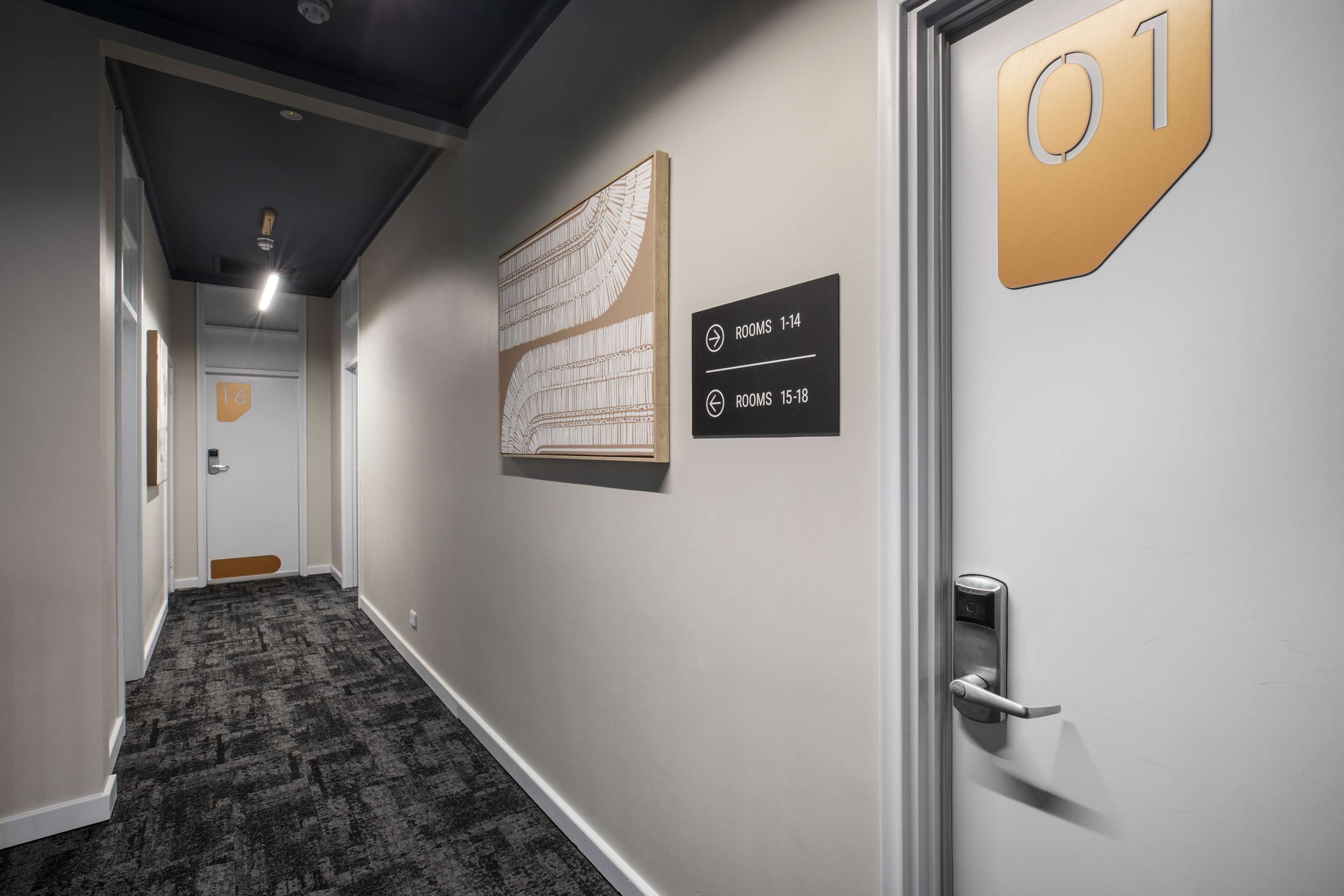 A hallway with a carpeted floor, a door labeled '01', and a sign indicating room numbers 1-14 and 15-18.