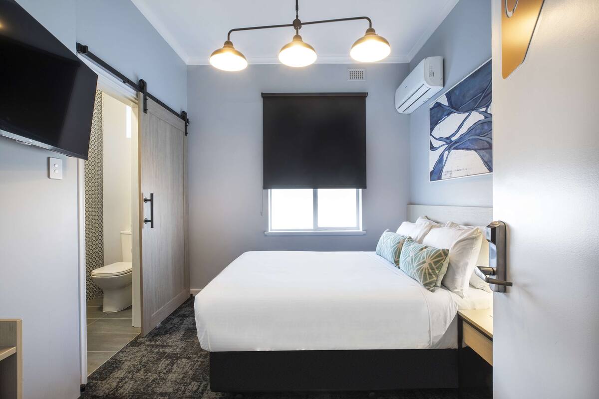 A bedroom with a bed, a window, a ceiling light, and a wall-mounted air conditioner.