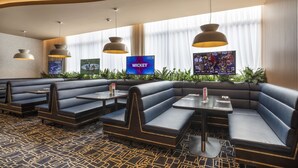 A modern restaurant with black cushioned booths and tables, large pendant lights, and a TV screen displaying a sports game. - Nightcap at Rex Hotel (Marleston)