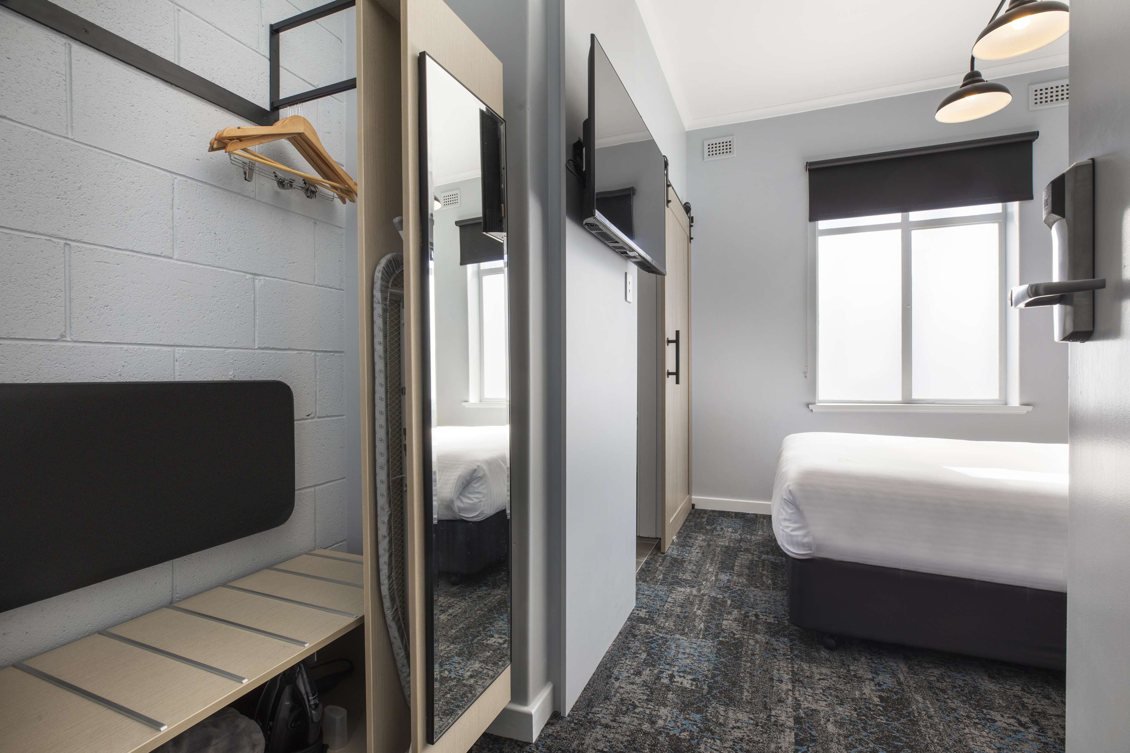 Quarto de hotel com cama, um banco, um espelho e uma janela.