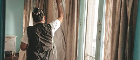 A person hanging a white garment on a curtain rod in a room with a window and a door.