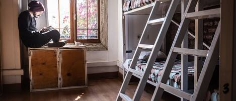 A room with a bunk bed, a ladder, and a person reading a book by a window.
