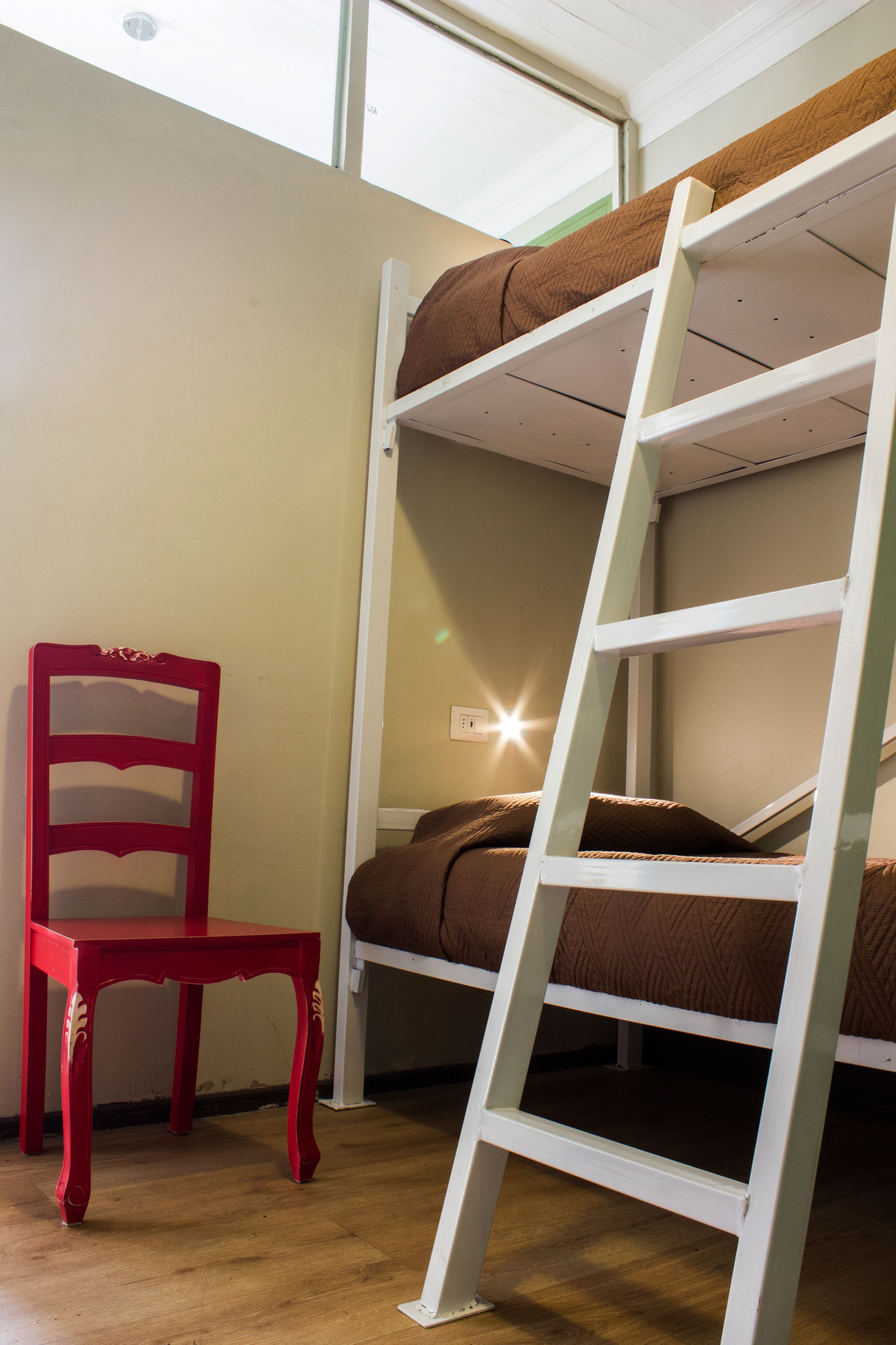A bunk bed with a ladder, a red chair, and a window with a light fixture.