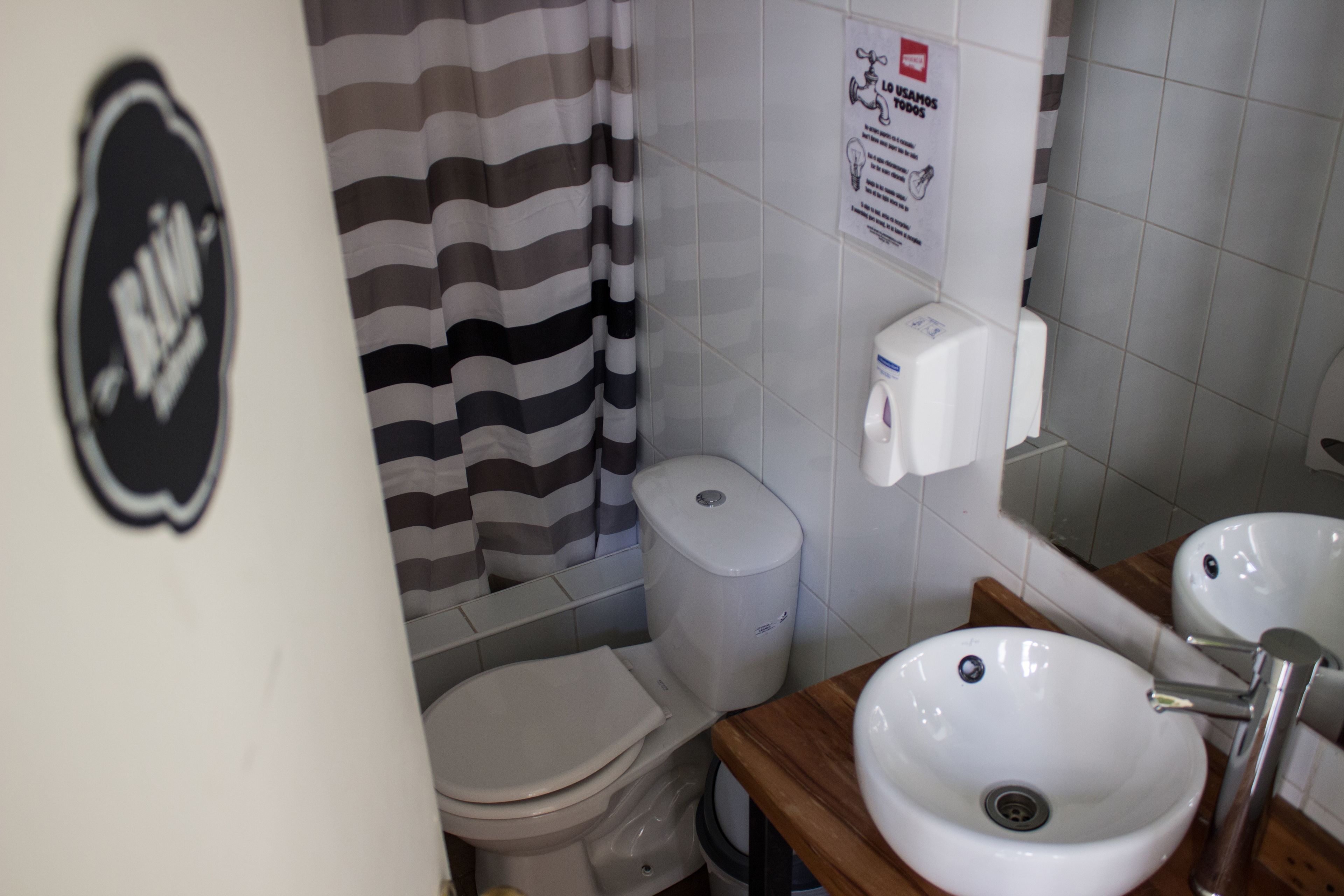 A bathroom with a striped shower curtain, a toilet, a sink, and a hand dryer.