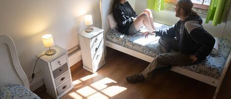 A small bedroom with a single bed, a bedside table with a lamp, and a window with curtains.