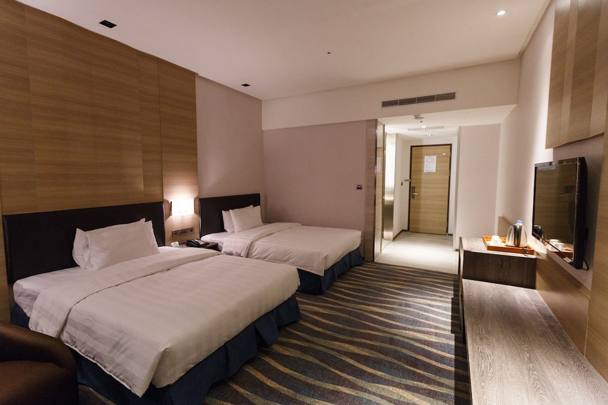 A hotel room with two beds, a TV, a desk, and a bathroom door.
