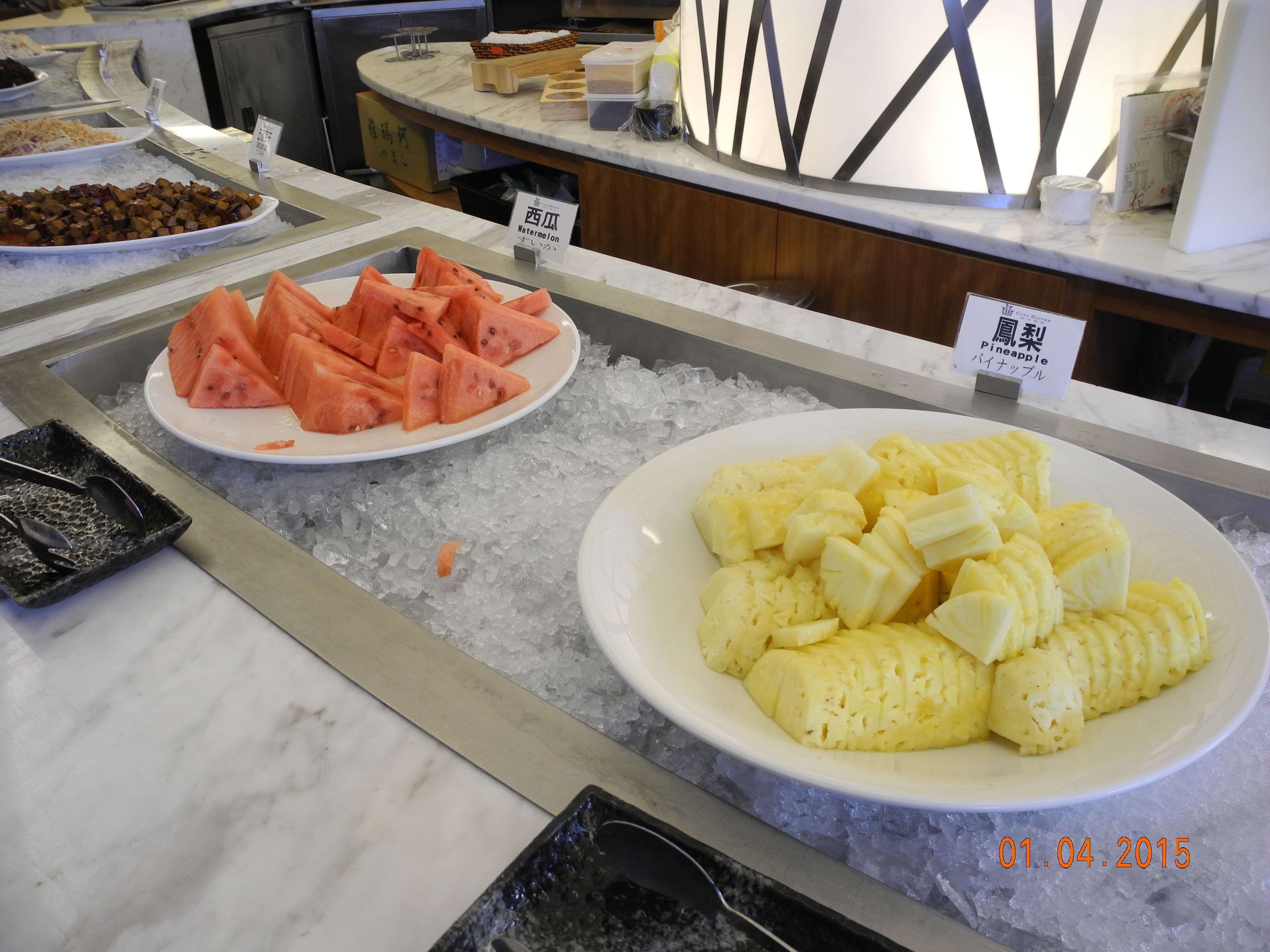 A buffet with plates of watermelon and pineapple slices on ice.
